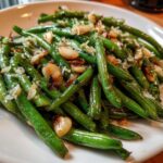 Close-up of vibrant green beans tossed in garlic butter and topped with toasted garlic slices.