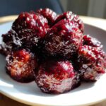 Close-up of savory grape jelly meatballs coated in a thick, glossy, dark red sauce.