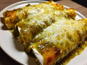 Close-up of three rolled green chile chicken enchiladas smothered in melted cheese on a white plate.