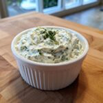 A close-up of creamy homemade tartar sauce, rich with herbs, served in a white fluted ramekin.
