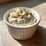 Close-up of creamy homemade tartar sauce recipe topped with chopped pickles in a white ramekin.