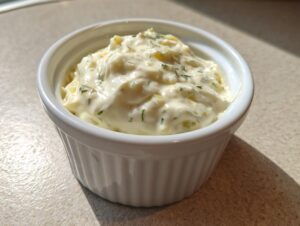 A close-up of creamy, homemade tartar sauce recipe speckled with green herbs and relish, served in a small white bowl.