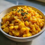 Close-up of sweet, glazed corn kernels coated in honey butter sauce, garnished with fresh thyme sprigs.