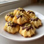 A plate of freshly baked italian butter cookies topped with melted chocolate and crushed pistachios.