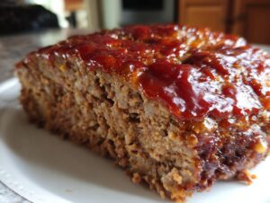 Close-up of a thick slice of juicy Keto meatloaf topped with a shiny, reddish-brown glaze.