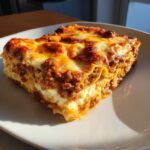 A close-up, appetizing slice of lasagna with cottage cheese, showing layers of pasta, meat sauce, and bubbly, browned cheese topping.