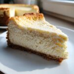 A close-up of a creamy slice of Keto cheesecake with a golden-brown crust on a white plate.