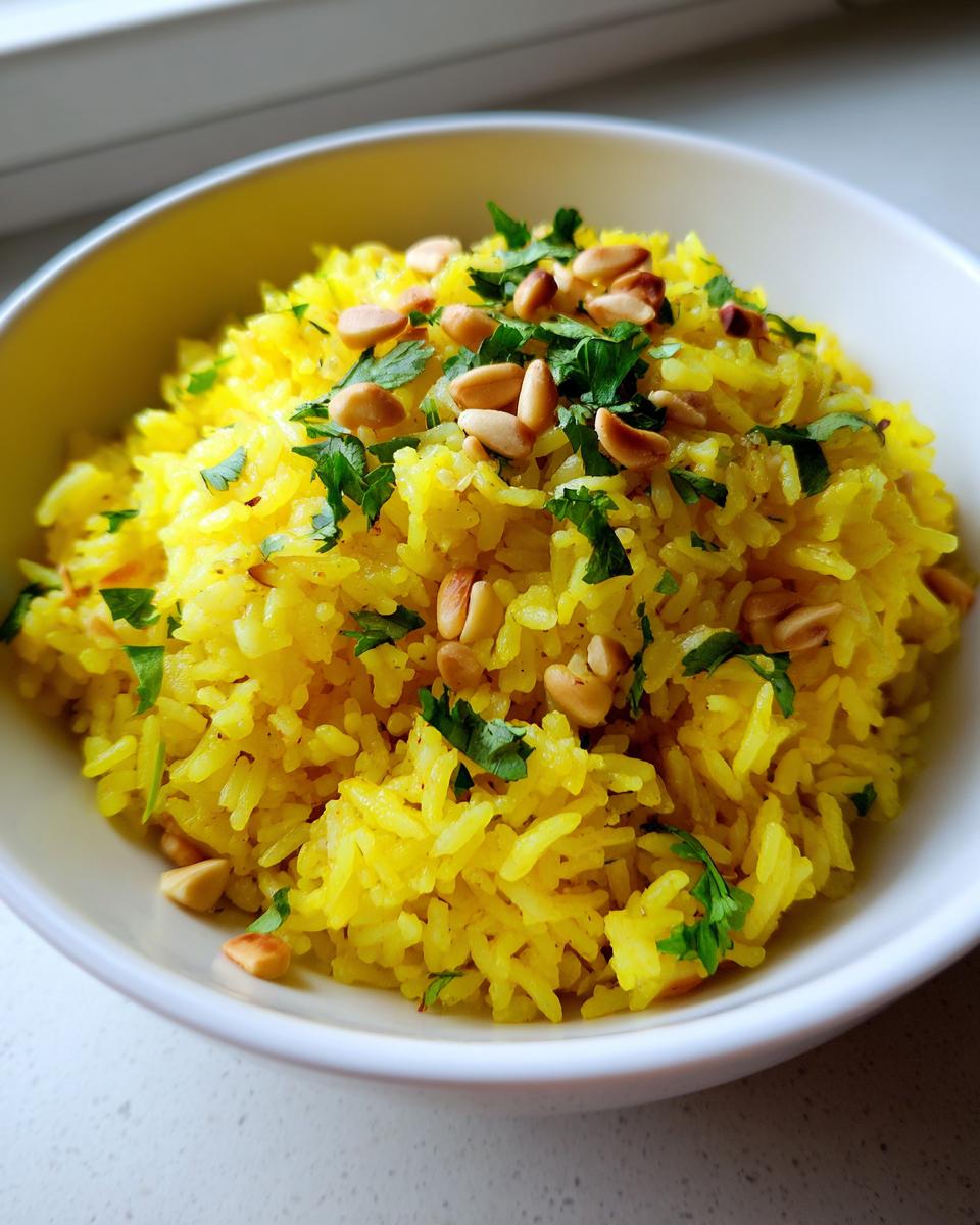 A close-up of vibrant yellow mediterranean rice topped with toasted pine nuts and fresh chopped parsley.