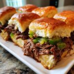 Close-up of several juicy Mississippi pot roast sliders filled with shredded beef and green peppers on a white platter.