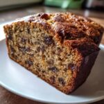 A close-up view of a moist slice of date nut bread showing raisins and walnuts baked inside.