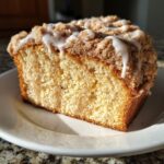 Close-up of a moist slice of coffee cake featuring a thick cinnamon streusel topping and a white vanilla glaze drizzle.