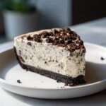 A thick slice of creamy, no-bake Oreo pie with a dark chocolate crust and crumbled topping.