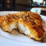 Close-up of a cooked parmesan crusted tilapia fillet broken open to show the moist, white interior.