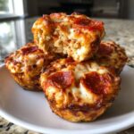 A stack of golden-brown, cheesy pepperoni pizza muffins, with one broken open to show the fluffy interior.