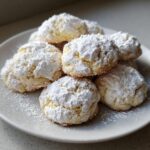 A stack of soft, crinkle-topped cool whip cookies generously dusted with powdered sugar on a white plate.