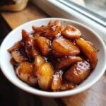 Close-up of thick, glossy, spiced apple pie filling slices in a small white bowl.