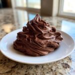 A mound of rich, dark chocolate frosting piped high on a white plate, showcasing deep swirls.
