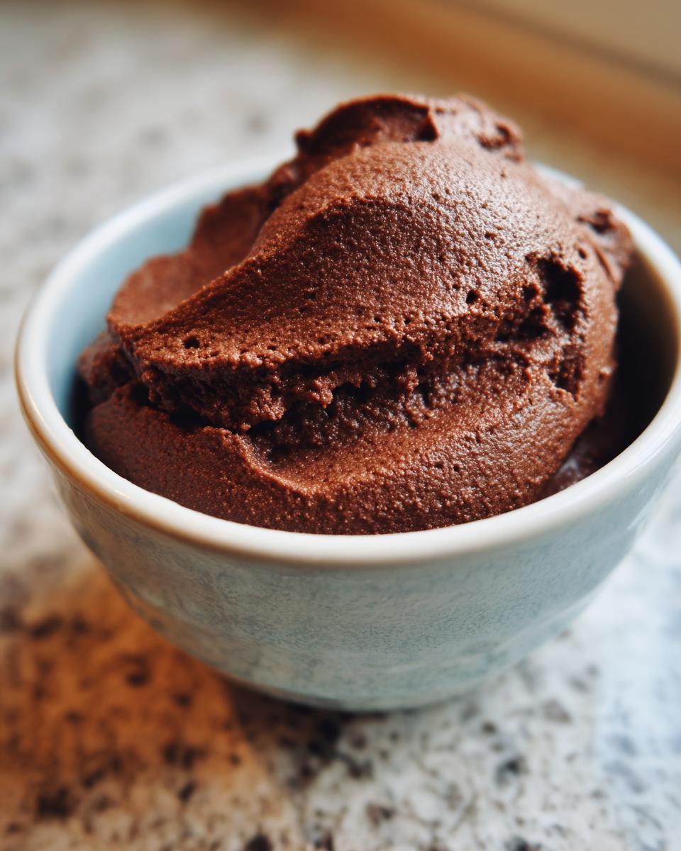 A close-up of rich, dark chocolate pudding scooped into a small, light blue ceramic bowl.