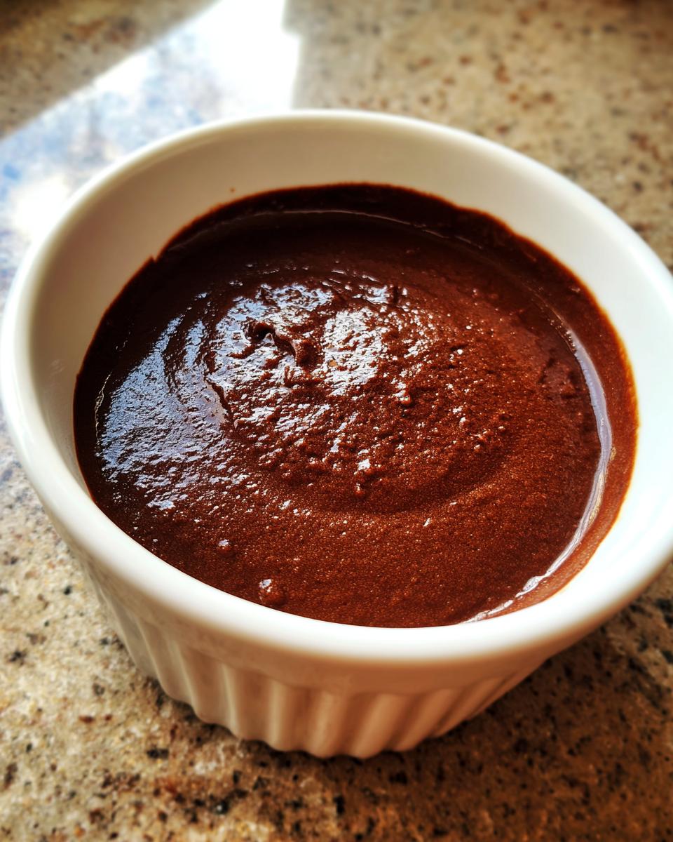 Close-up of rich, dark chocolate pudding served in a white fluted ramekin on a speckled countertop.