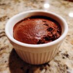 A close-up of rich, dark chocolate pudding served in a small, white, fluted ramekin.