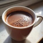 Close-up of rich, dark hot chocolate topped with small bubbles in a white mug.