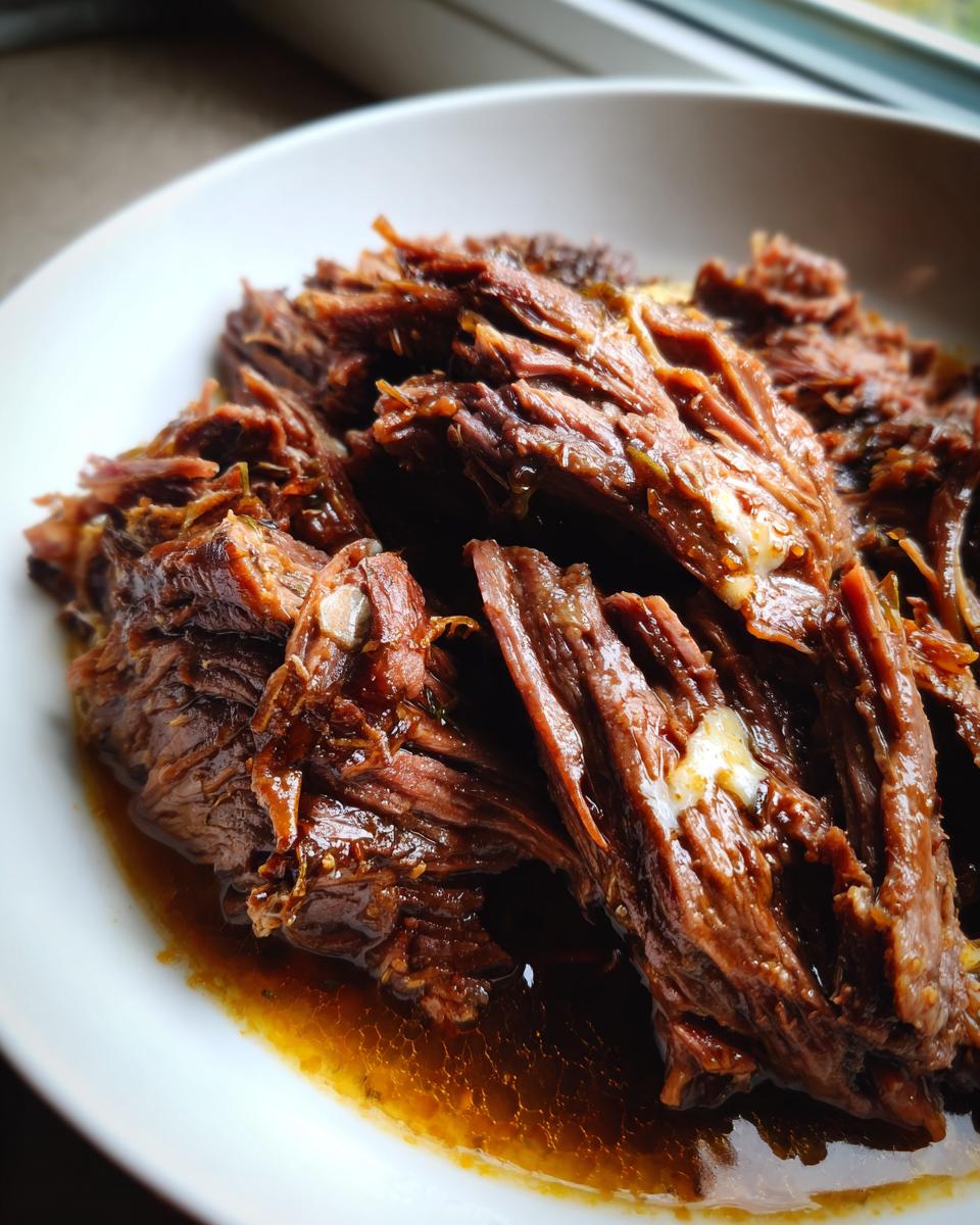Close-up of tender, shredded mississippi pot roast served in a white bowl with its rich brown juices.
