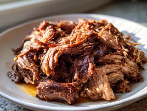 Close-up of perfectly shredded, juicy mississippi pot roast piled high on a white plate.