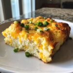 A close-up serving of fluffy sheet pan eggs topped with melted cheddar cheese and fresh green onions.