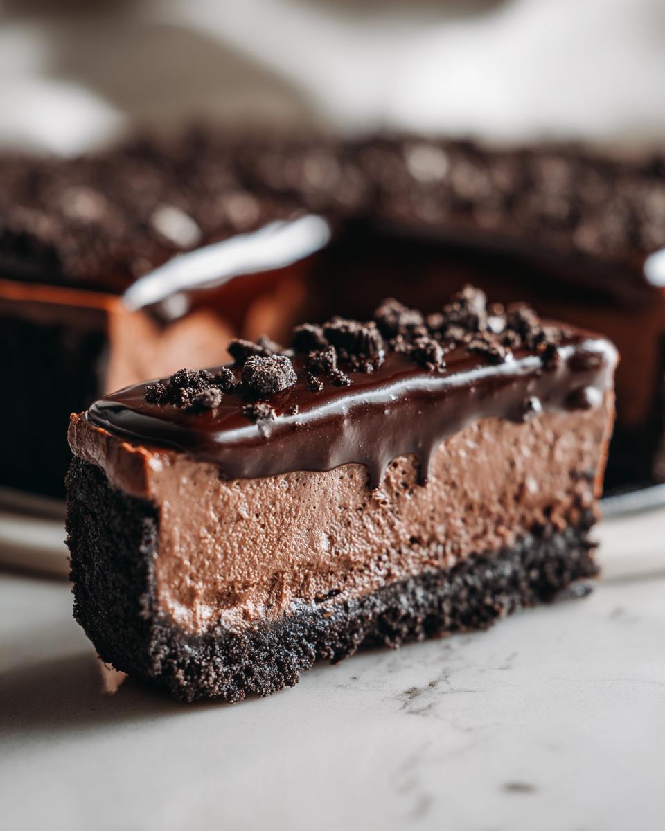 Close-up of a slice of chocolate mousse pie showing a dark cookie crust, light brown mousse filling, and chocolate ganache topping.