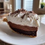 A decadent slice of Christmas chocolate cream pie showing two layers of chocolate filling, topped with whipped cream and chocolate shavings.