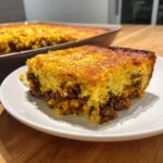 A thick slice of cowboy cornbread casserole showing a golden top crust and a savory ground meat and corn filling.