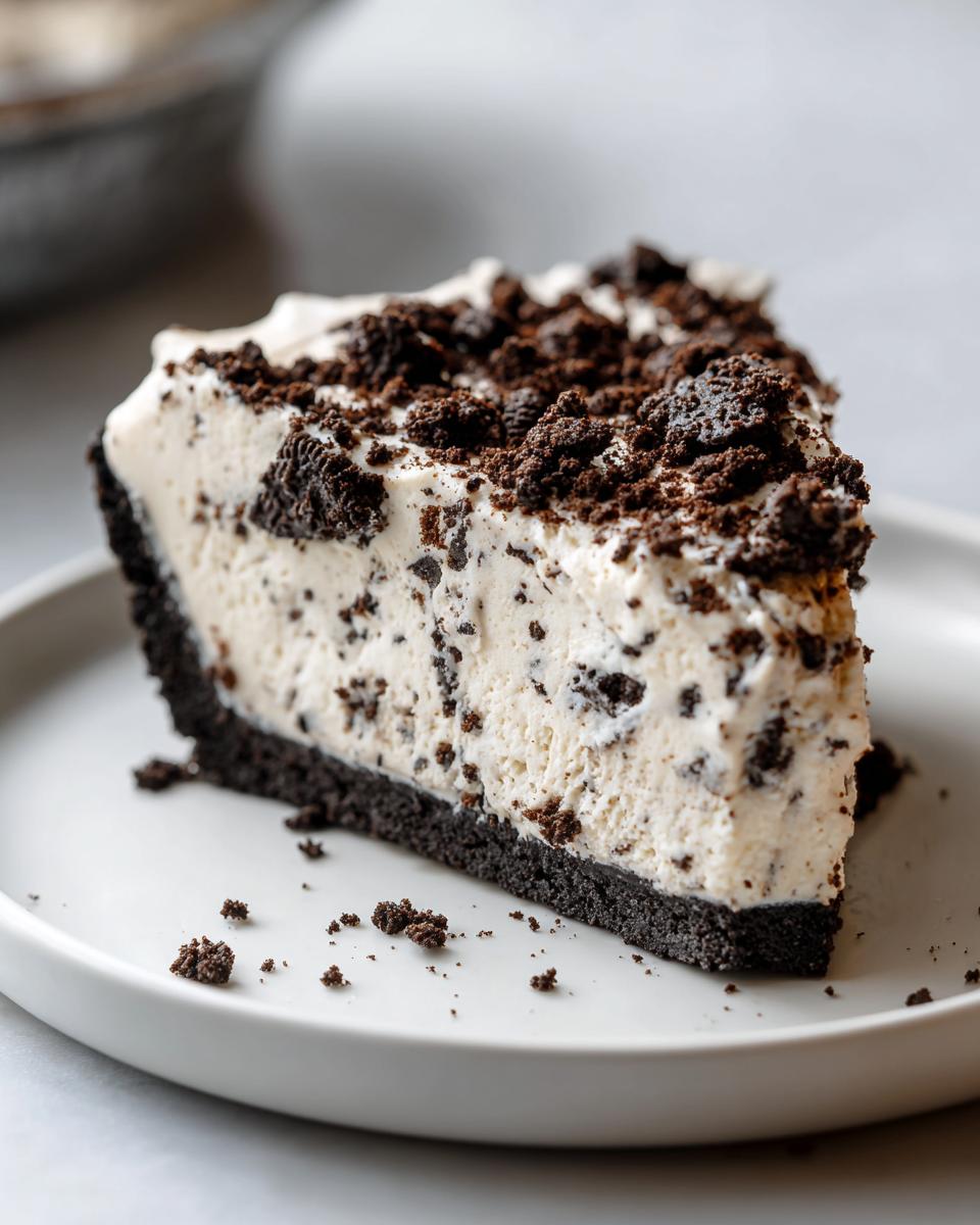 A close-up slice of creamy, no-bake Oreo pie with a dark chocolate crust and crumbled topping.