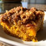 A close-up of a rich, moist slice of pumpkin pecan cobbler showing the orange filling and crunchy pecan topping.