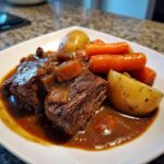 Two pieces of tender slow cooker pot roast smothered in rich brown gravy with carrots and potatoes.