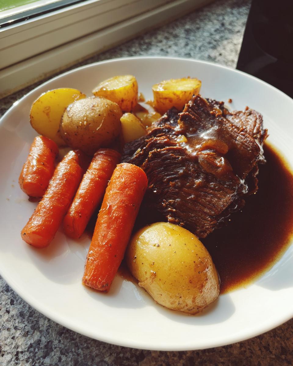 A serving of tender slow cooker pot roast covered in rich gravy, alongside whole carrots and small potatoes.