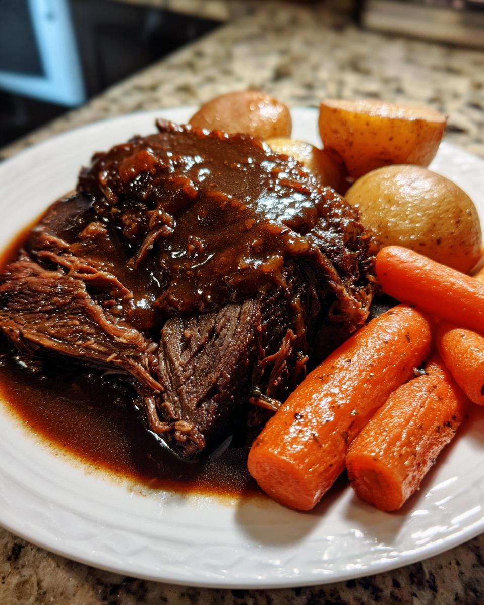 A plate featuring tender, shredded slow cooker pot roast covered in rich brown gravy, served with carrots and potatoes.