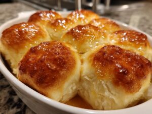 Close-up of soft, golden-brown buttery rolls baked together in a white dish and covered in a shiny glaze.