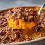 A spoonful of creamy orange southern sweet potato casserole topped with a crunchy pecan streusel topping.