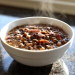 Close-up of a white bowl filled with hot, steaming black eyed peas cooked with chunks of ham.