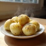 A plate piled high with steaming hot potato dumplings seasoned with pepper and herbs.