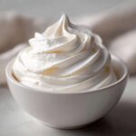 Close-up of stiff, white frosting piped into a swirl in a small white bowl, representing the texture of royal icing recipe.