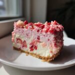 Close-up of a perfect slice of strawberry crunch cheesecake showing the graham cracker crust and strawberry swirl.