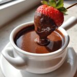 A fresh strawberry being dipped into a small white bowl of rich, melted chocolate fondue.