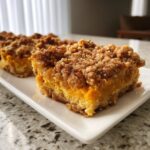 Close-up of two slices of rich, orange sweet potato casserole bars topped with a thick, brown streusel crumble.