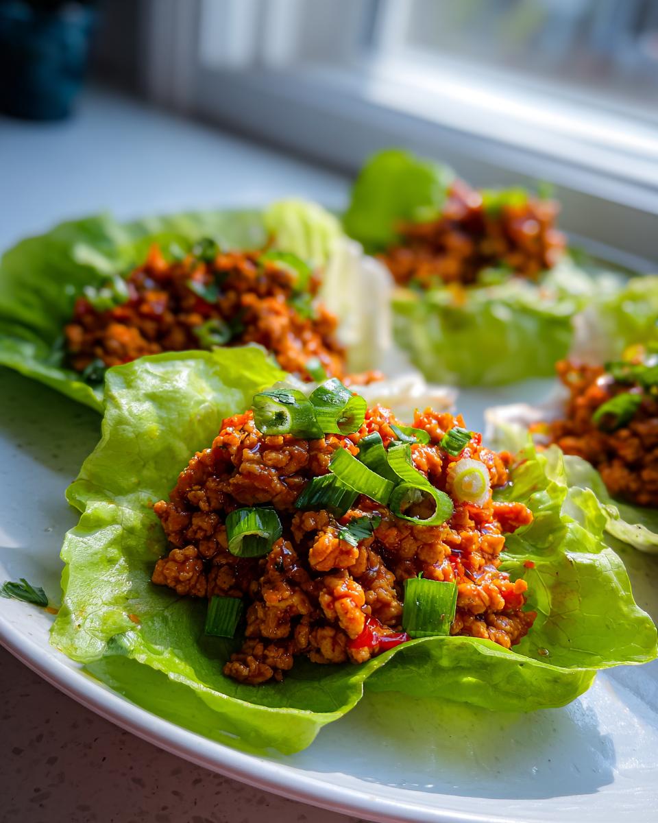 Close-up of several thai chicken lettuce wraps filled with savory ground chicken and topped with fresh green onions.