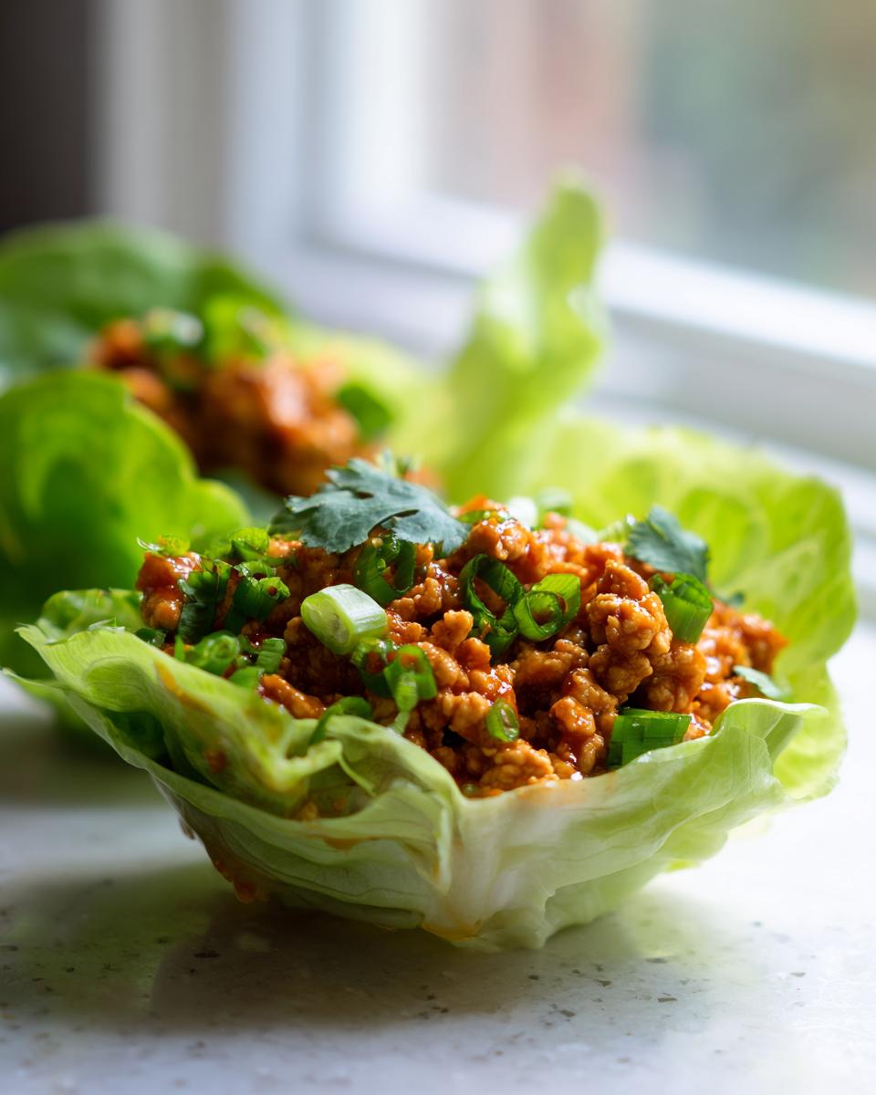 A vibrant close-up of thai chicken lettuce wraps filled with savory ground chicken mixture, topped with green onions and cilantro.