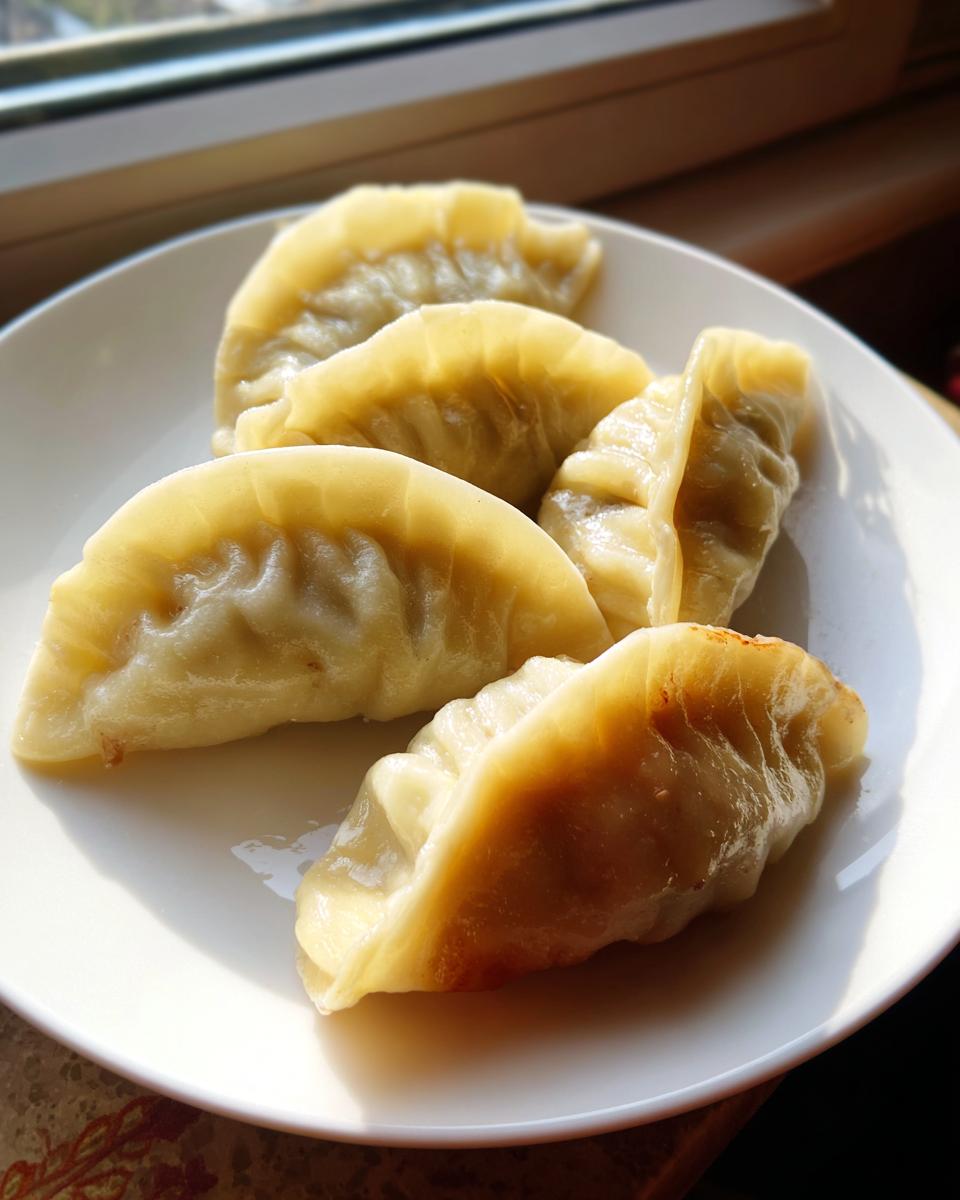 Close-up of five pan-fried Traditional Chinese Dumplings with golden bottoms resting on a white plate near a window.