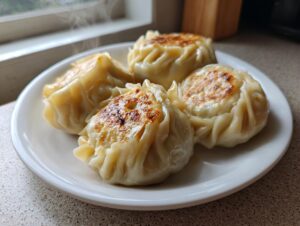 Four freshly cooked, steaming Traditional Chinese Dumplings with golden-brown seared bottoms served on a white plate.
