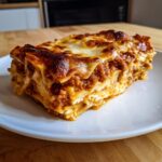 A hearty, golden-brown slice of ultimate lasagna showing layers of pasta, rich meat sauce, and creamy cheese.