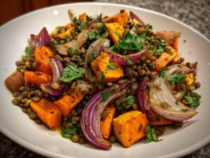A close-up of a hearty veggie lentil salad featuring roasted sweet potatoes, red onions, and green lentils, garnished with parsley.